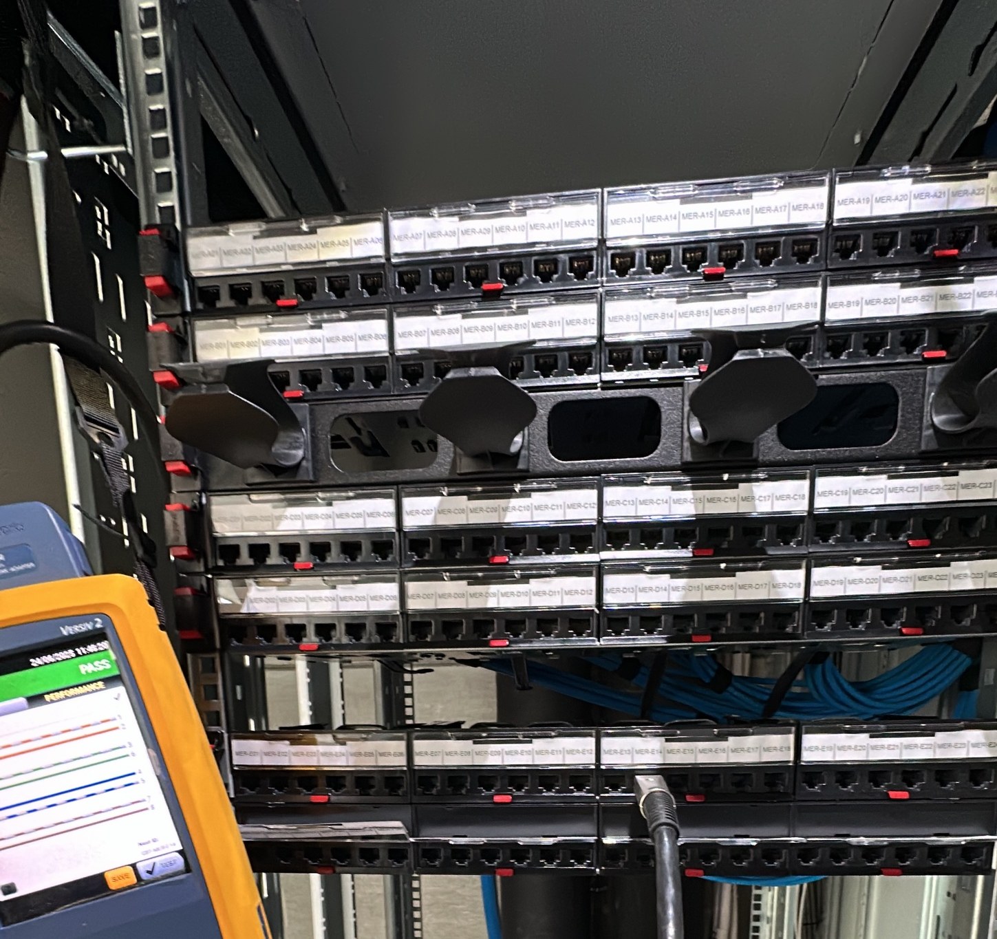 Fluke DSX certificeringstester met PASS-resultaat, aangesloten op een gelabeld patchpaneel