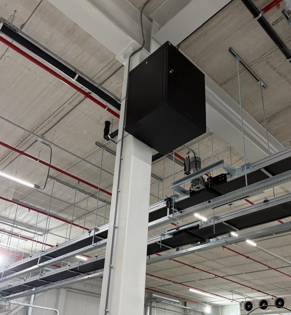 Zwarte wandkast hoog op een kolom in een productiehal, boven de kabelgoten
